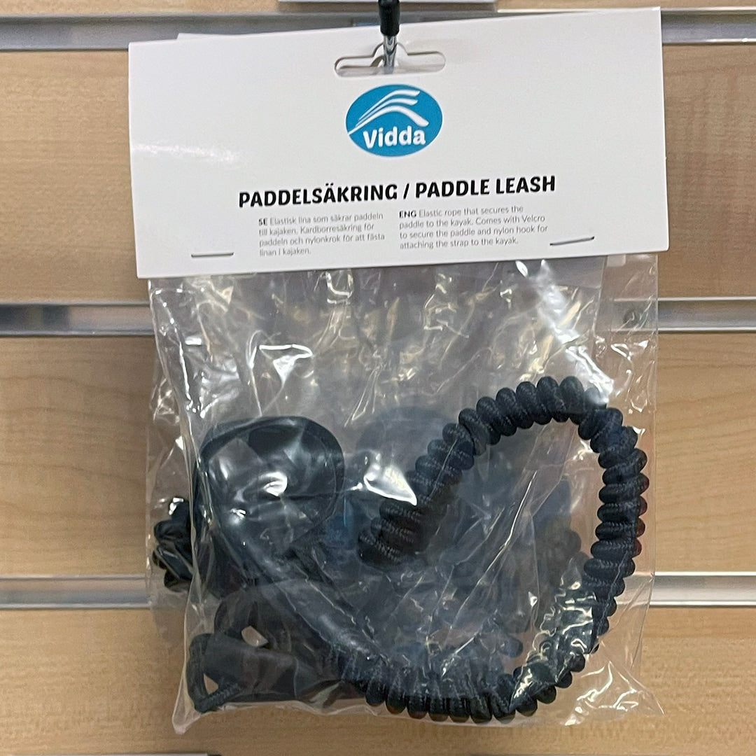 Förpackad paddelsäkring/leash från Vidda. Svart spiralsnöre med karbinhake och kardborreband för att säkra paddeln till kajaken