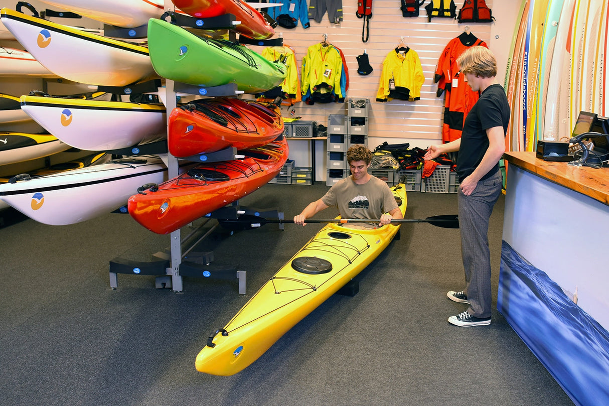 En kund provar en gul Seabird Expedition-havskajak inne i en butik, med butiksinredning synlig runt omkring.