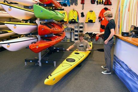 En kund provar en gul Seabird Expedition-havskajak inne i en butik, med butiksinredning synlig runt omkring.