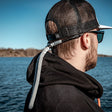 Leech flytsnöre/glasögonsnodd i grått material fäst vid solglasögonen på en man som bär keps vid vattnet