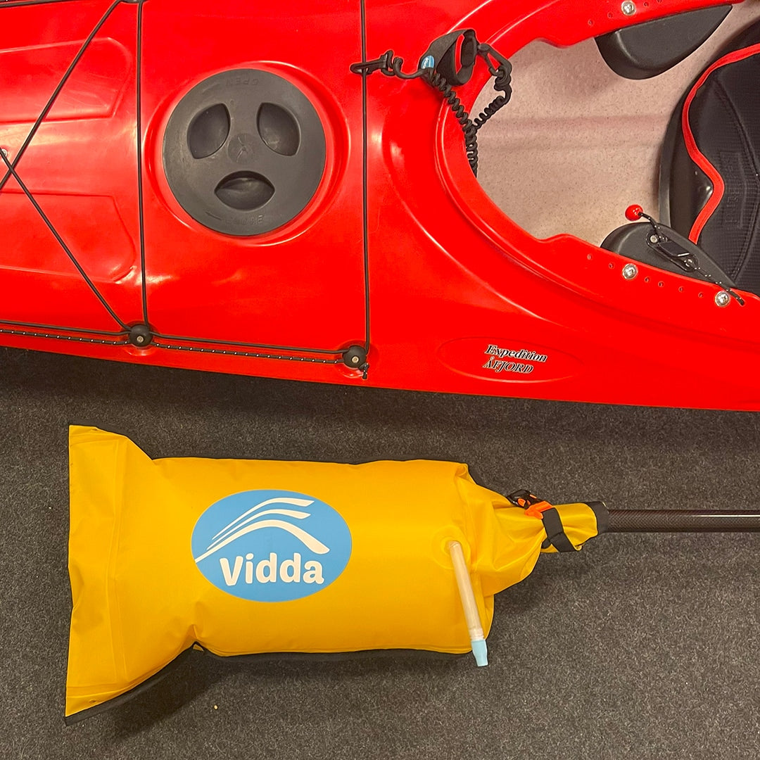 Gul, uppblåsbar Vidda paddelflottör/reservstabilisator ligger framför en röd kajak (Expedition Åfjord) för att visa säkerhetsutrustning