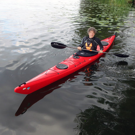 En röd Seabird Expedition-plastkajak paddlas på lugnt vatten,