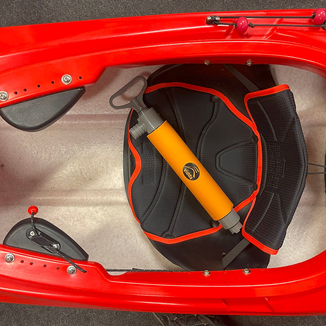 Orange Vidda länspump inuti en röd Seabirdkajak, ligger på den svarta och orangea sätet. Visar sittbrunnen och lårstöd