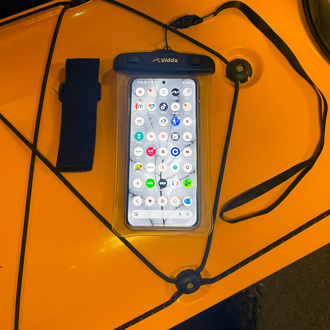 Vidda phonecase med en påslagen mobiltelefon inuti, ligger säkrad med ett svart snöre på däck på en gul Seabird glasfiberkajak